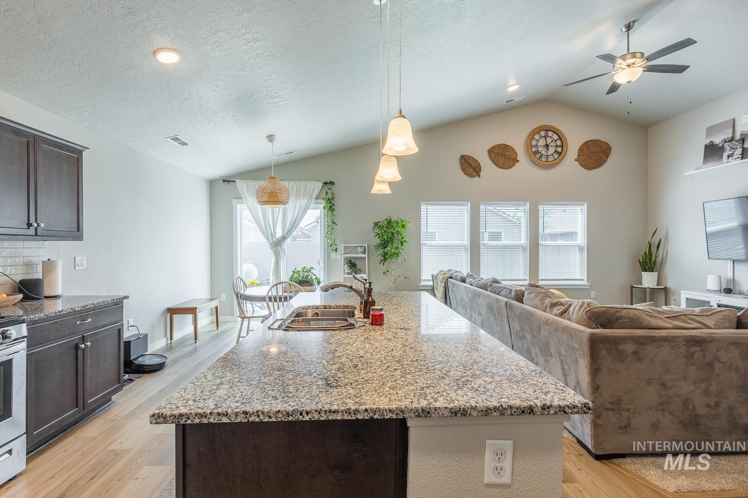 12623 Shadow Peak Street Caldwell, ID 83607 - Photo 19 of 50 Open-concept living space featuring a vaulted ceiling, wood-finish flooring, a kitchen island with stone-finish countertop, and a ceiling fan