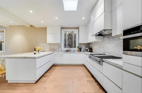 a large white kitchen with stainless steel appliances granite countertop a stove and a sink