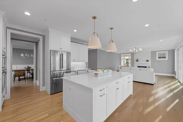 a large kitchen with kitchen island a stove a sink a refrigerator and white cabinets with wooden floor