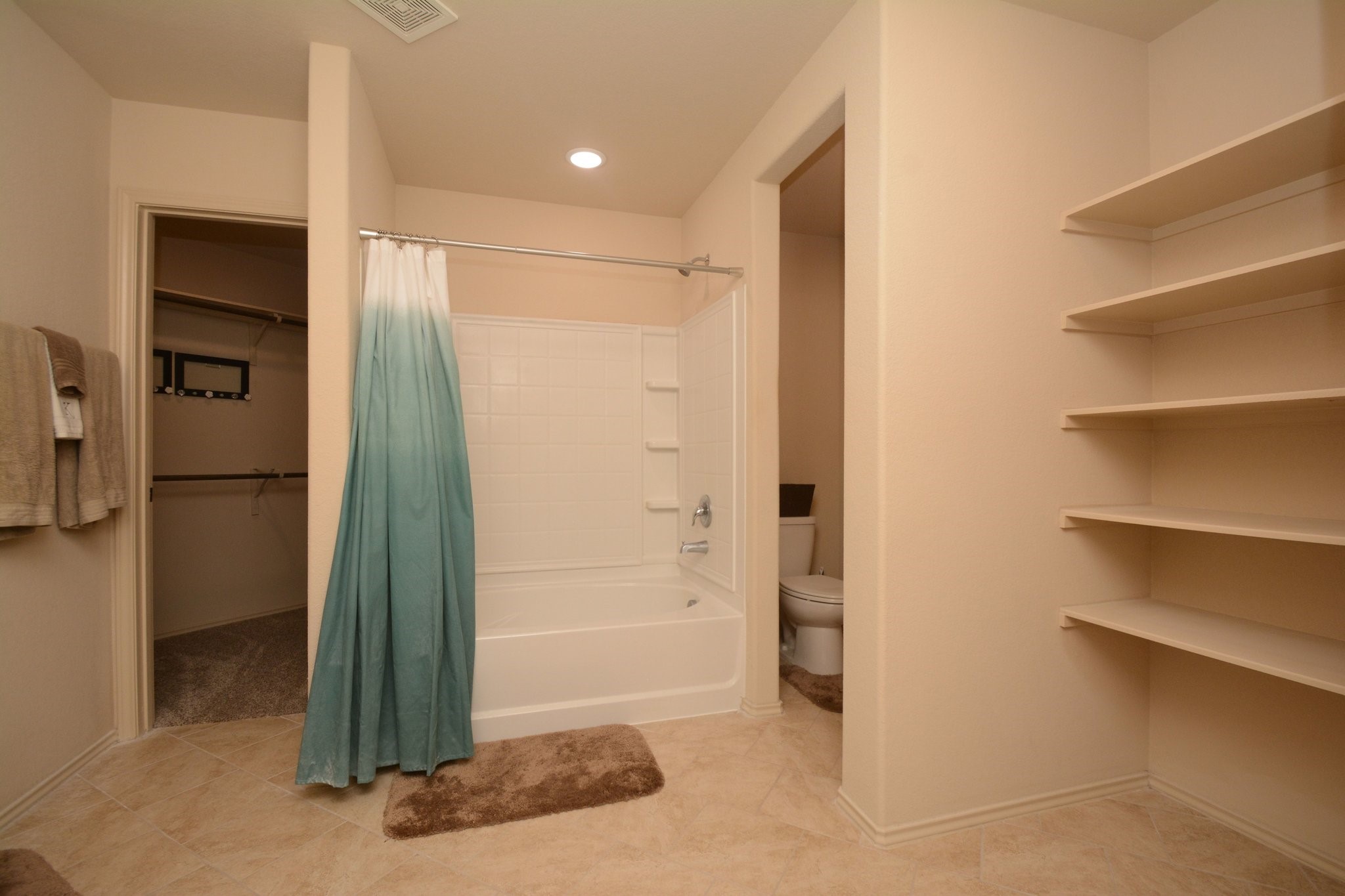 23318 Dukes Run Drive Spring, TX 77373 - Photo 28 of 41 This bathroom features a tub with a shower, neutral tiles, built-in shelving, and access to a walk-in closet. The space is well-lit and offers a clean, minimalist design.