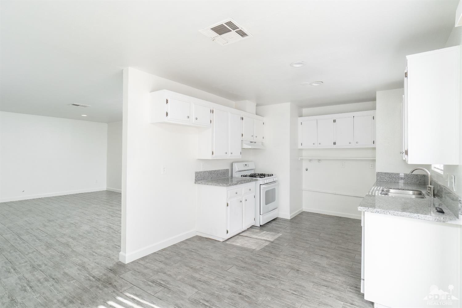 66186 Santa Rosa Road Desert Hot Springs, CA 92240 - Photo 2 of 23 a kitchen with granite countertop a refrigerator a sink a stove and white cabinets