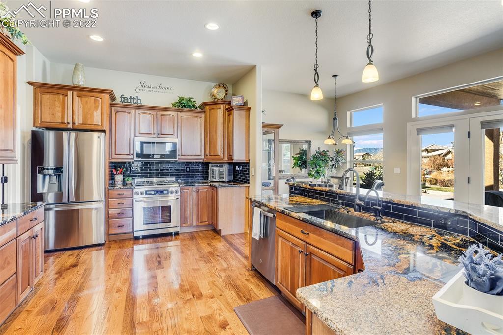 13214 Cake Bread Heights Colorado Springs, CO 80921 - Photo 8 of 28 a large kitchen with stainless steel appliances kitchen island granite countertop a refrigerator a stove a sink dishwasher a dining table and chairs with wooden floor