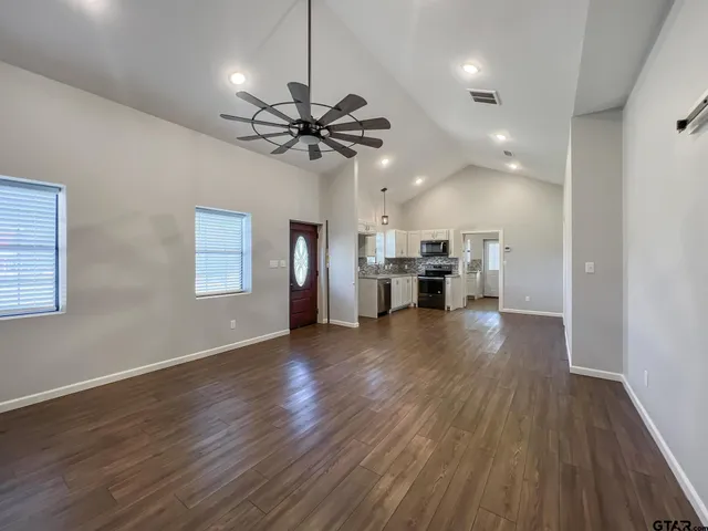 a view of an empty room and a kitchen with wooden floor a ceiling fan