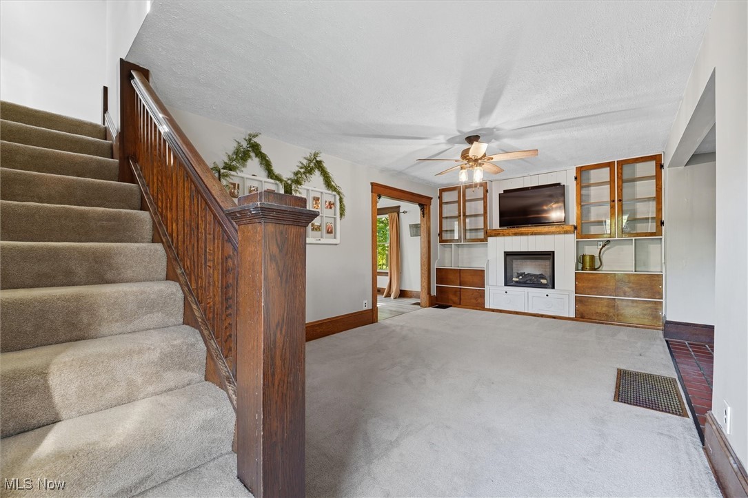 10536 Johnnycake Ridge Road Painesville, OH 44077 - Photo 11 of 40 Carpeted living room with ceiling fan, a textured ceiling, stairs, and a fireplace