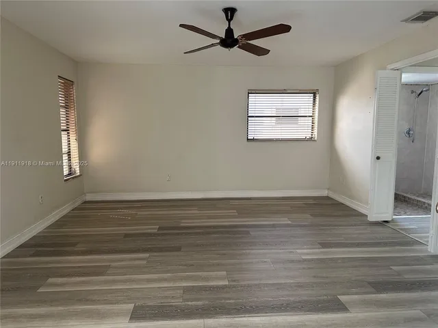 a view of empty room with wooden floor and fan