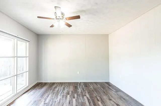 an empty room with wooden floor fan and windows