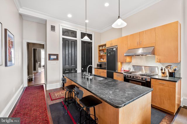 a kitchen with stainless steel appliances granite countertop a refrigerator a sink dishwasher and a dining table with wooden floor