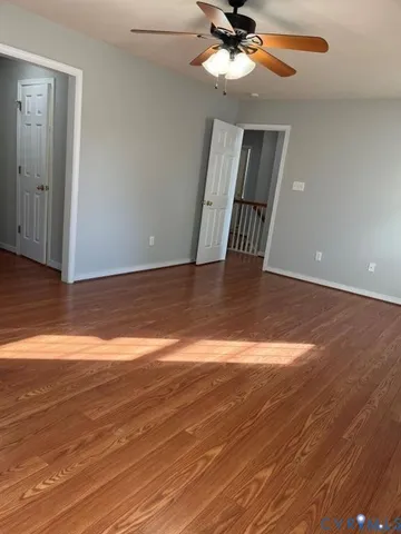 a view of an empty room with wooden floor and a ceiling fan