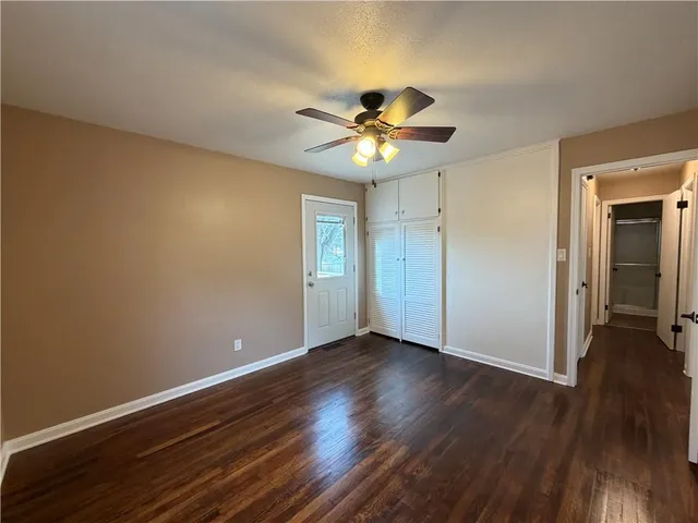 a view of an empty room with wooden floor and a ceiling fan