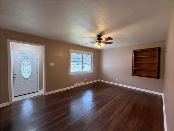 an empty room with wooden floor chandelier fan and windows