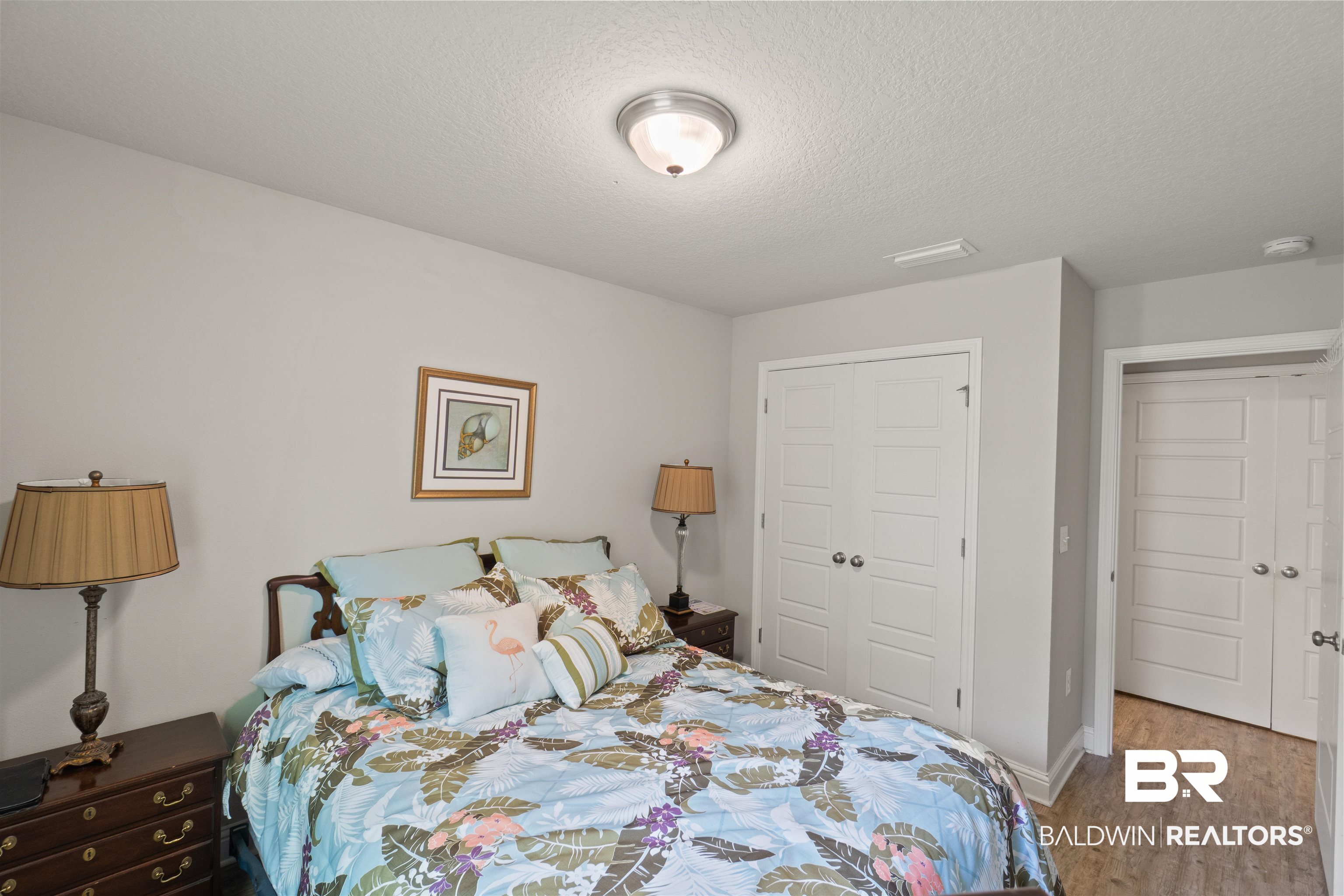 25806 Pollard Road, Unit 6 Daphne, AL 36526 - Photo 20 of 38 Bedroom with light gray wall paint, wood-finish flooring, two paneled closet doors, and a ceiling-mounted light fixture