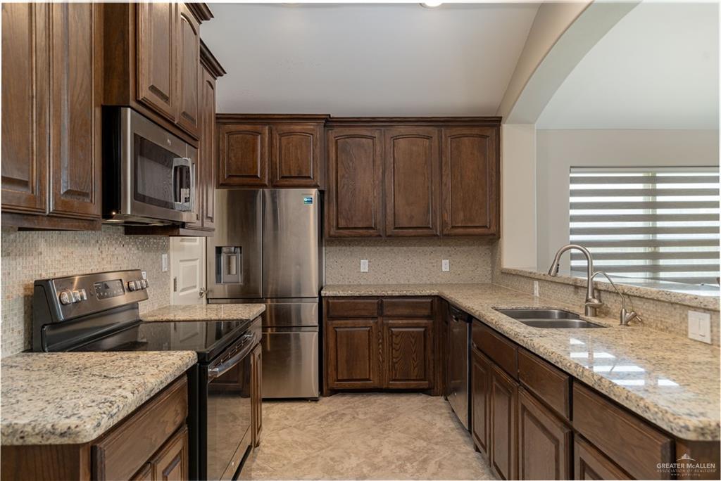 412 South Paseo Del Rey Street Mission, TX 78572 - Photo 4 of 15 Kitchen with stainless steel appliances, backsplash, light stone countertops, and dark brown cabinetry