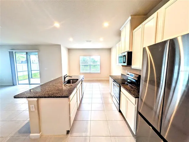 a living room with stainless steel appliances furniture a flat screen tv and a kitchen view