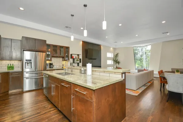 a kitchen with stainless steel appliances granite countertop a refrigerator a sink dishwasher a oven and a dining table with wooden floor