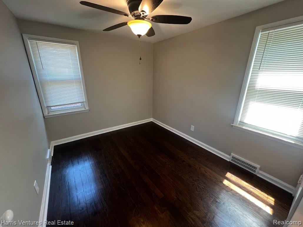 22148 Moross Road Grosse Pointe, MI 48236 - Photo 13 of 16 Room featuring dark wood-finish flooring, two windows with blinds, a ceiling fan with integrated lighting, and neutral wall tones
