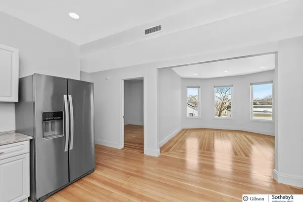 a view of empty room with wooden floor and kitchen