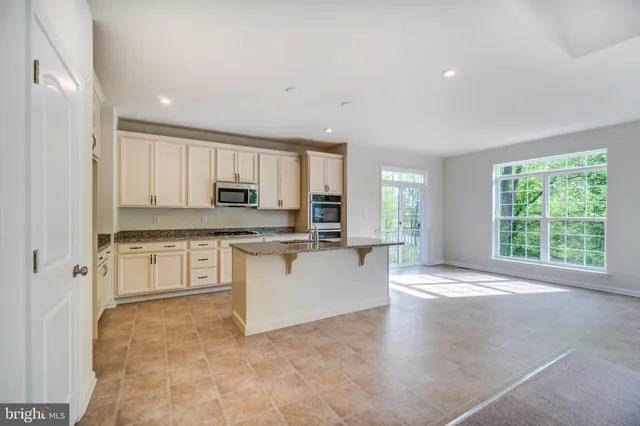 a large white kitchen with granite countertop a stove a sink a window and stainless steel appliances