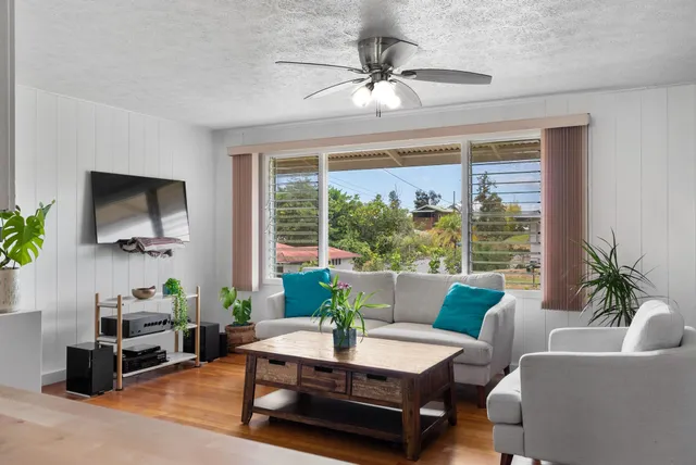 a living room with furniture a ceiling fan a flat screen tv and a large window