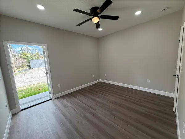 an empty room with wooden floor fan and windows