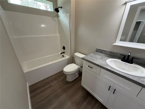a bathroom with a granite countertop sink a toilet a mirror and bathtub