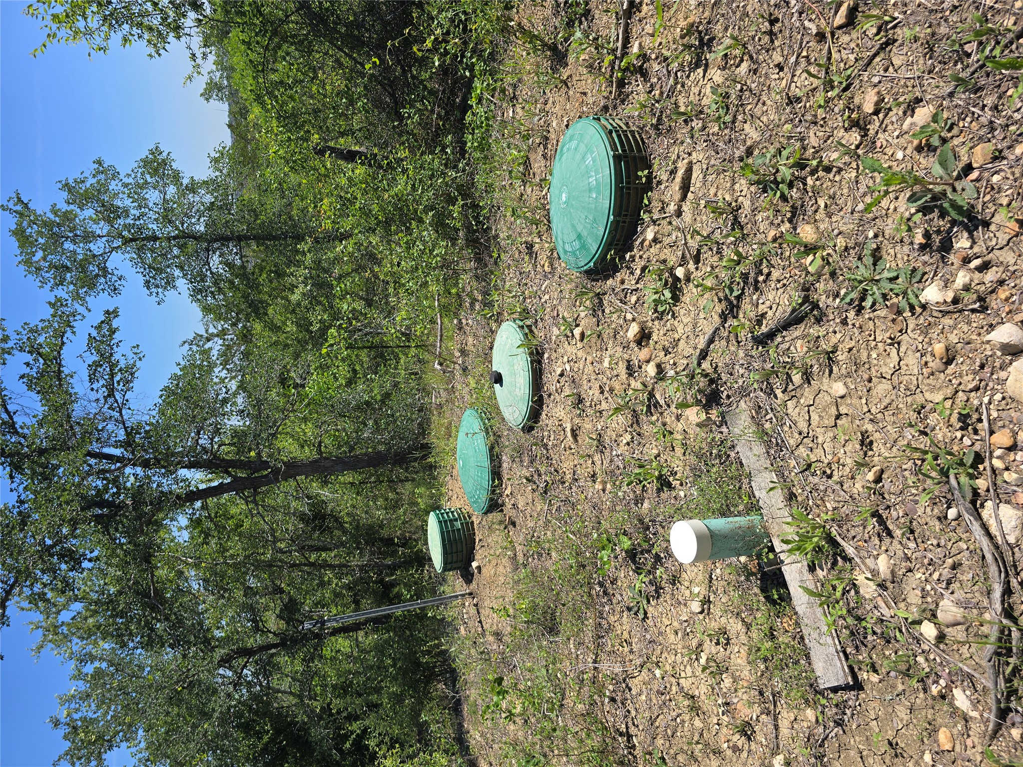 693 Santa Teresa Road Kyle, TX 78640 - Photo 18 of 20 Green covers dot a verdant landscape, hinting at subterranean utilities amid lush natural surroundings.