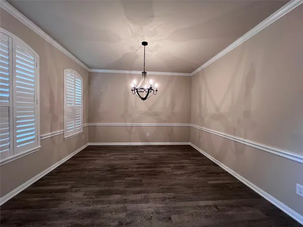 an empty room with wooden floor chandelier and windows