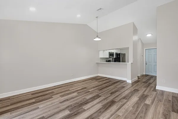 an empty room with wooden floor and kitchen view
