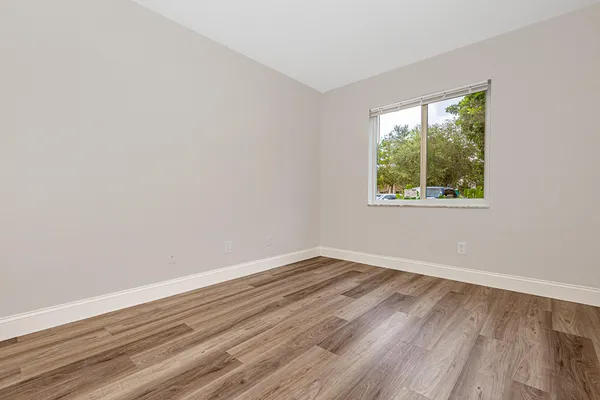 a view of an empty room with wooden floor and a window