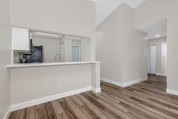a view of an empty room with wooden floor and a kitchen