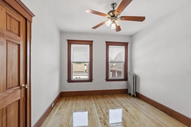 an empty room with wooden floor chandelier fan and windows
