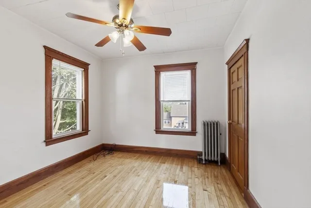 an empty room with wooden floor chandelier fan and windows