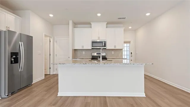 a kitchen with stainless steel appliances granite countertop a refrigerator a sink a stove a microwave and white cabinets with wooden floor