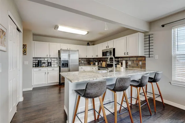 a kitchen with stainless steel appliances kitchen island granite countertop a refrigerator a stove a sink and white cabinets with wooden floor