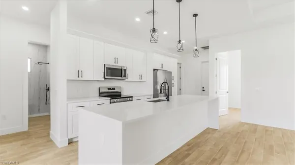 a kitchen with stainless steel appliances a refrigerator a sink dishwasher a oven with white cabinets and wooden floor