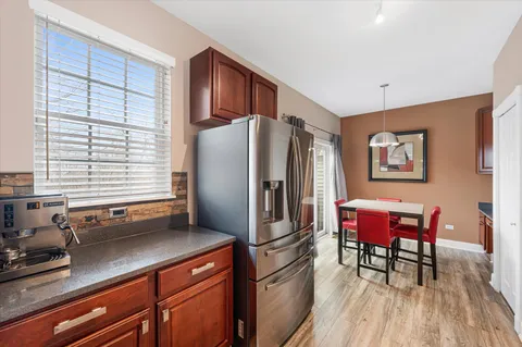a kitchen with stainless steel appliances granite countertop a refrigerator a sink dishwasher a dining table and chairs with wooden floor