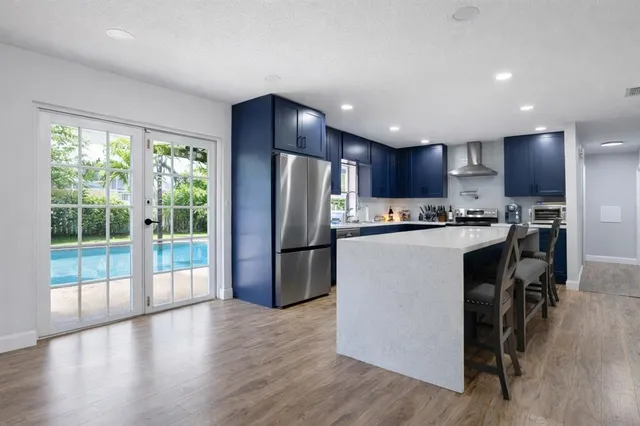 a kitchen with stainless steel appliances a refrigerator a stove a kitchen island hardwood floor and a large window