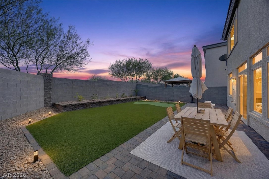 10446 Emerald Rye Street Las Vegas, NV 89183 - Photo 32 of 37 An inviting backyard oasis offers a private putting green and patio space under a vibrant twilight sky.