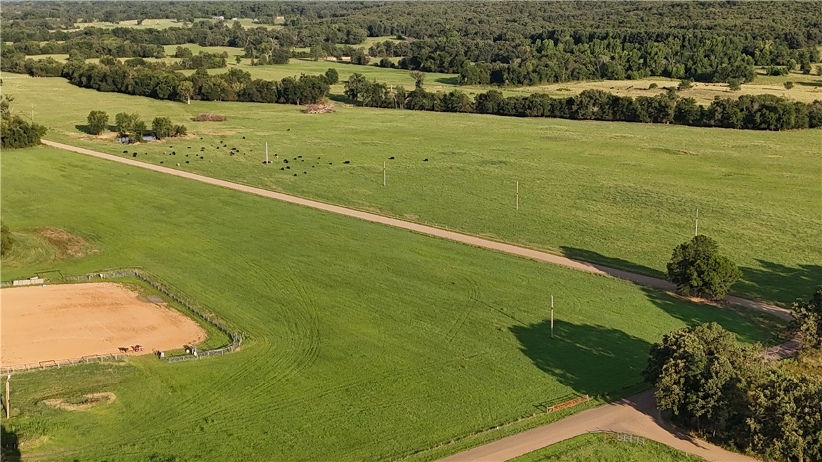2210 Weiterer Road Scranton, AR 72863 - Photo 43 of 49 Expansive green pastures featuring a perimeter of mature trees, a dedicated riding arena, and a winding unpaved road