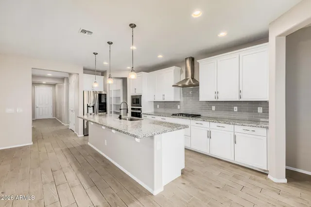 a large kitchen with stainless steel appliances kitchen island granite countertop a stove a sink a refrigerator and white cabinets with wooden floor