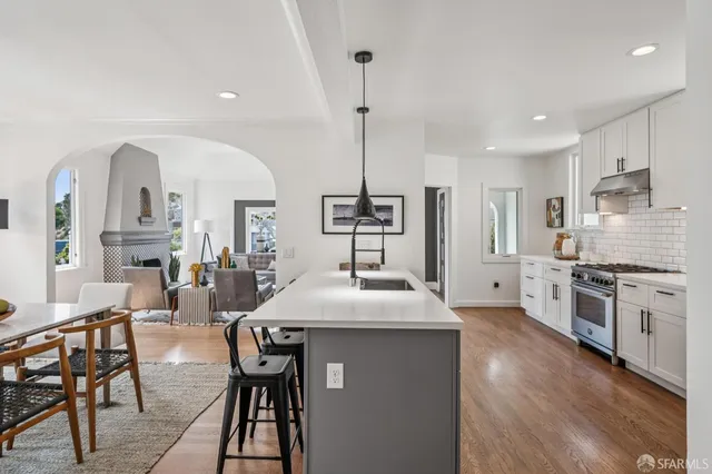 a kitchen with stainless steel appliances kitchen island granite countertop a stove a sink and white cabinets with wooden floor