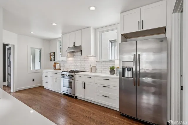 a kitchen with stainless steel appliances granite countertop a sink a refrigerator and a wooden floor