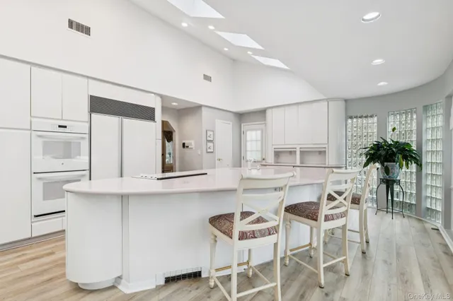 a kitchen with stainless steel appliances kitchen island granite countertop a stove a refrigerator and white cabinets with wooden floor