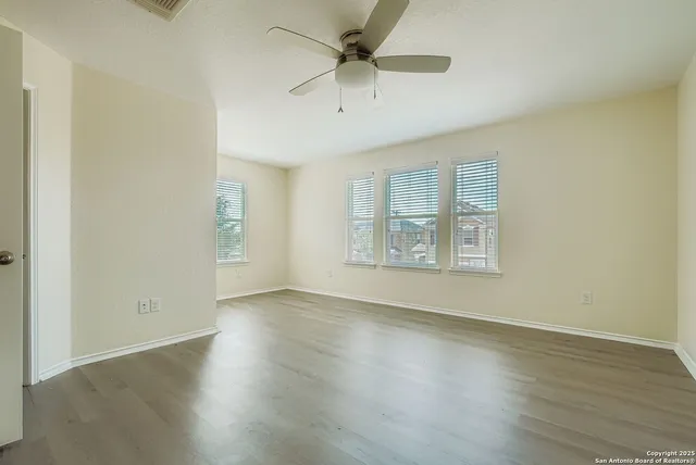 an empty room with wooden floor chandelier fan and windows