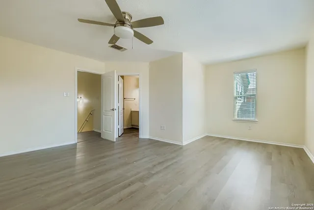 an empty room with wooden floor ceiling fan and windows