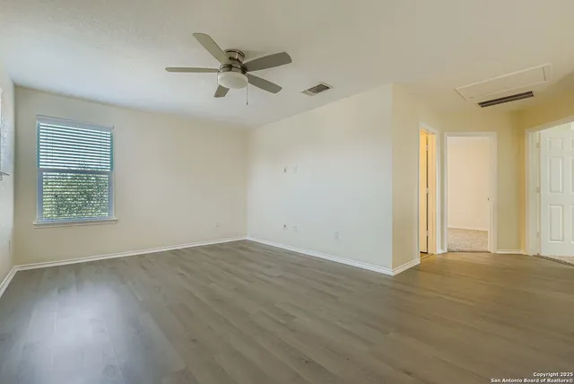 an empty room with wooden floor fan and windows
