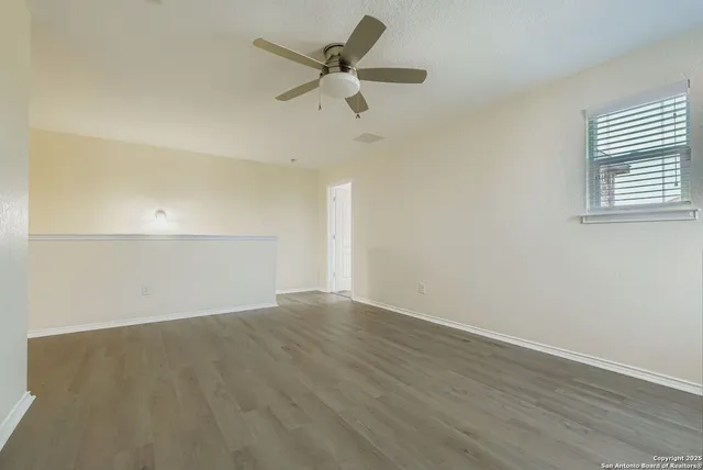 an empty room with wooden floor fan and windows