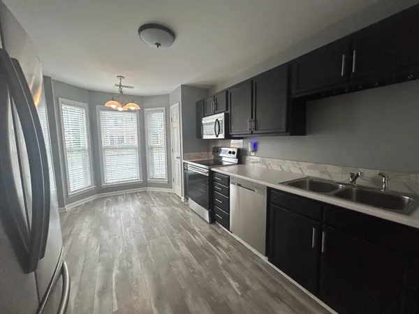 a kitchen with stainless steel appliances granite countertop a refrigerator a sink dishwasher a stove and white countertops with wooden floor