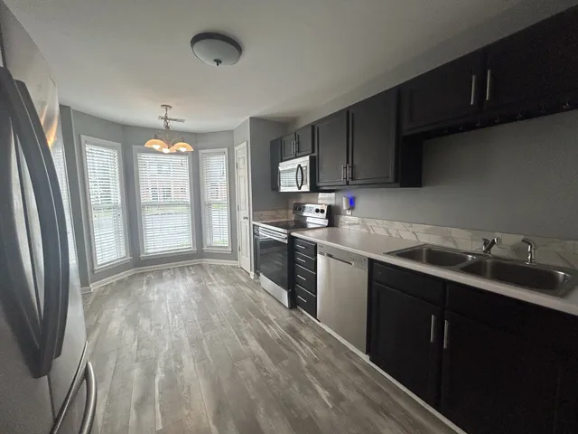 a kitchen with stainless steel appliances granite countertop a refrigerator a sink dishwasher a stove and white countertops with wooden floor