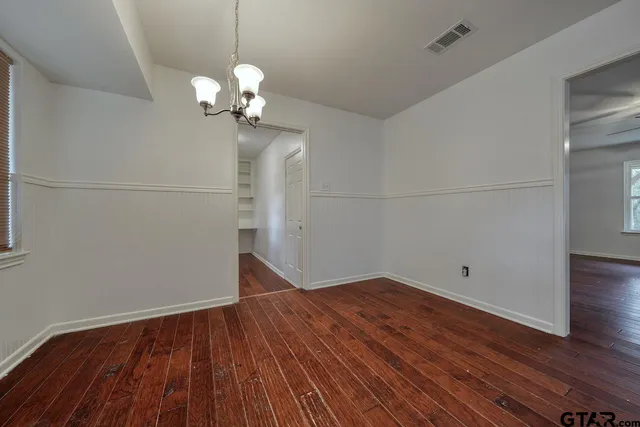 an empty room with wooden floor chandelier fan and windows