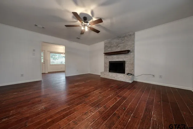 a view of an empty room with wooden floor fireplace and a window